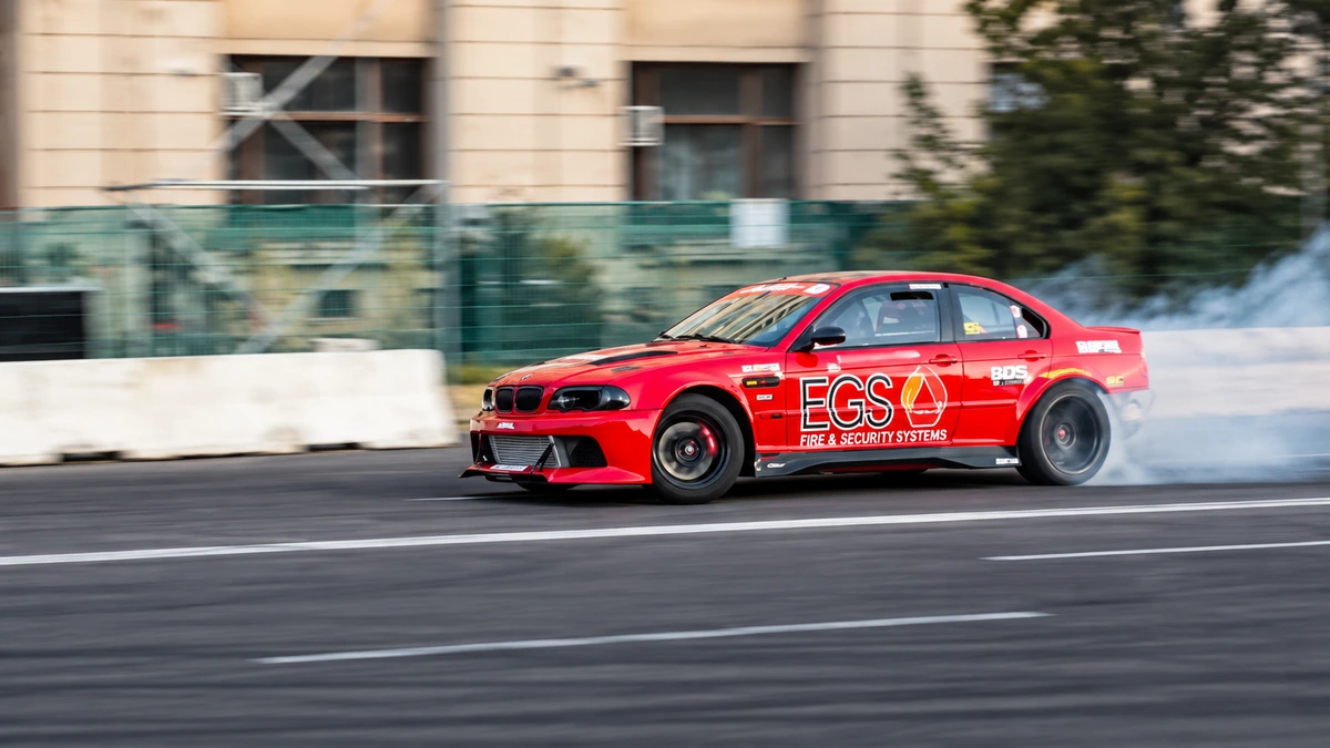 BMW roșu de competiție în derapaj pe circuit, cu fum de la anvelope.