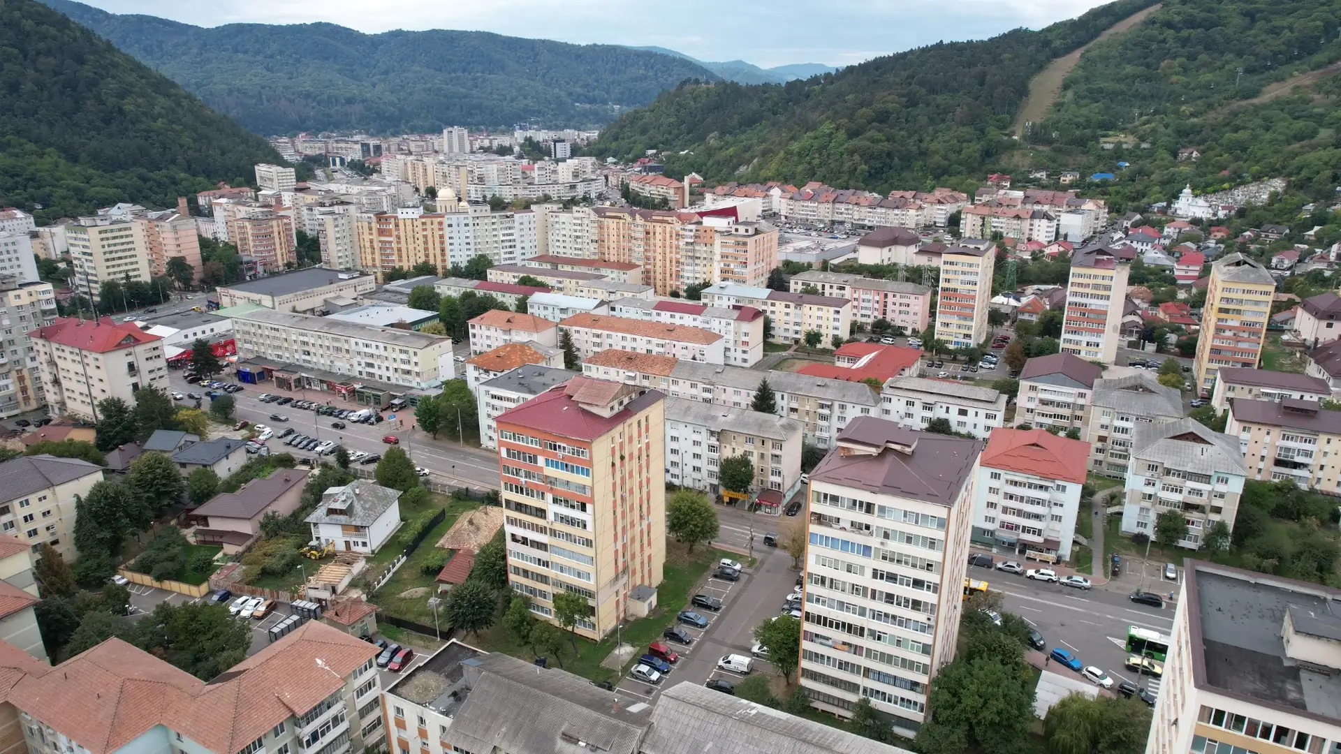 Vedere aeriană asupra unor blocuri de locuințe cu balcoane închise, între dealuri împădurite